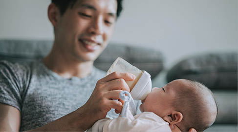 Asian Chinese young father feeding his baby boy son with milk bottle at living room during weekend
